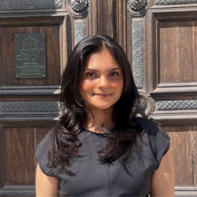 Agrima Singh, smiling outside a wooden doorway in Sweden